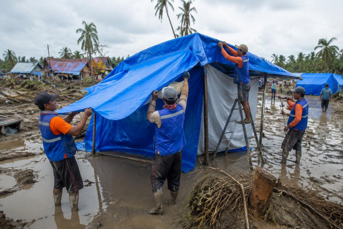 Relief workers installing PVC tarpaulin shelters in post-flood site