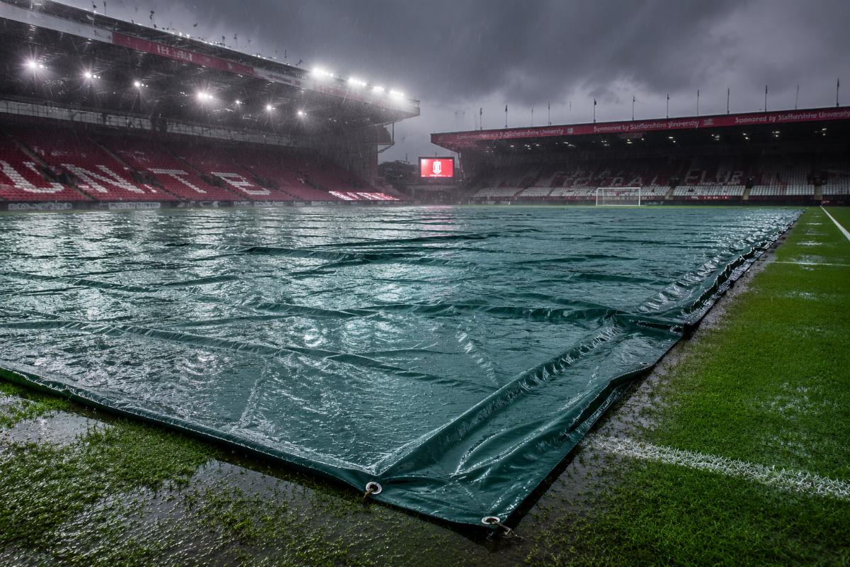 Sports ground cover tarpaulin laid across a wet football pitch during a rainstorm
