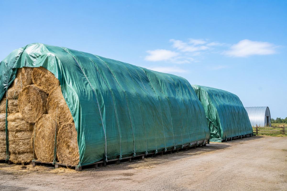 Well-secured hay bales covered by durable woven PE tarps in an open farm storage yard